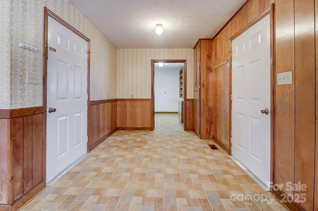 hallway with a textured ceiling and wood walls