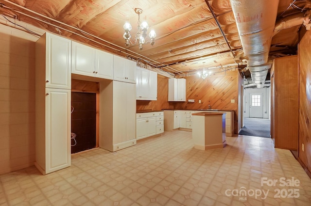 kitchen featuring an inviting chandelier, decorative light fixtures, wooden walls, a kitchen island, and white cabinets