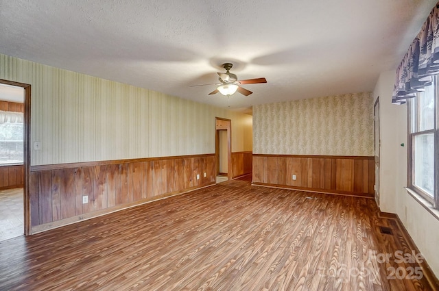 empty room with ceiling fan, wood-type flooring, a textured ceiling, and plenty of natural light