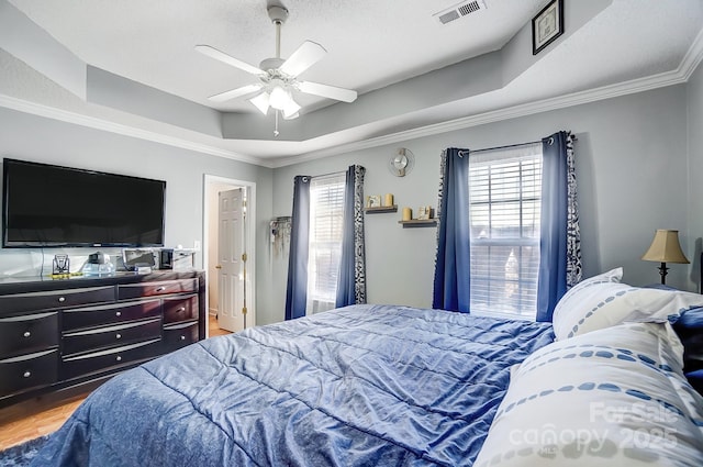 bedroom with ceiling fan, a tray ceiling, and multiple windows