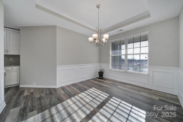 unfurnished dining area featuring ornamental molding, dark wood-type flooring, a chandelier, and a raised ceiling