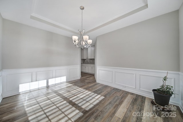 unfurnished dining area featuring an inviting chandelier, a tray ceiling, and dark hardwood / wood-style flooring