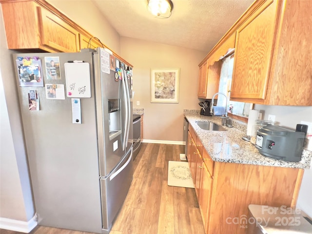 kitchen featuring appliances with stainless steel finishes, sink, light wood-type flooring, light stone countertops, and a textured ceiling