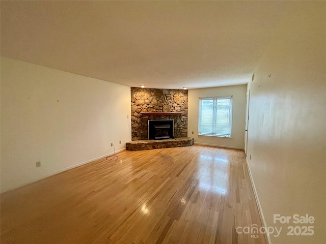 unfurnished living room with wood-type flooring and a stone fireplace