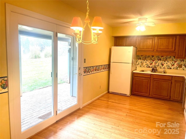 kitchen with sink, decorative light fixtures, a chandelier, light hardwood / wood-style flooring, and white fridge