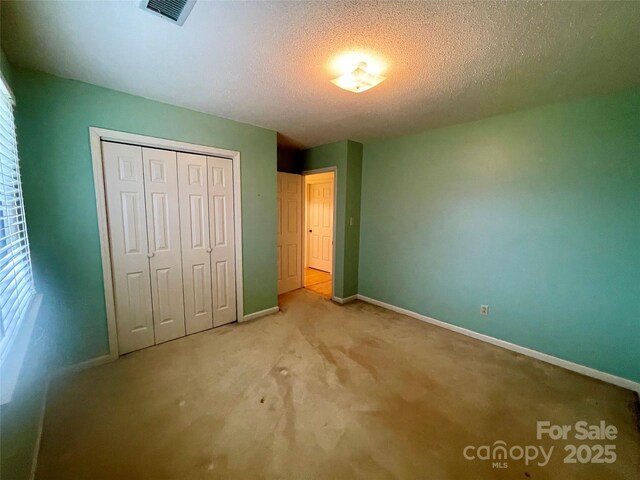 unfurnished bedroom featuring light carpet, a closet, and a textured ceiling