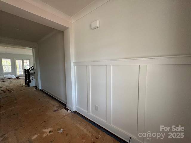 hall with a wainscoted wall, ornamental molding, and a decorative wall