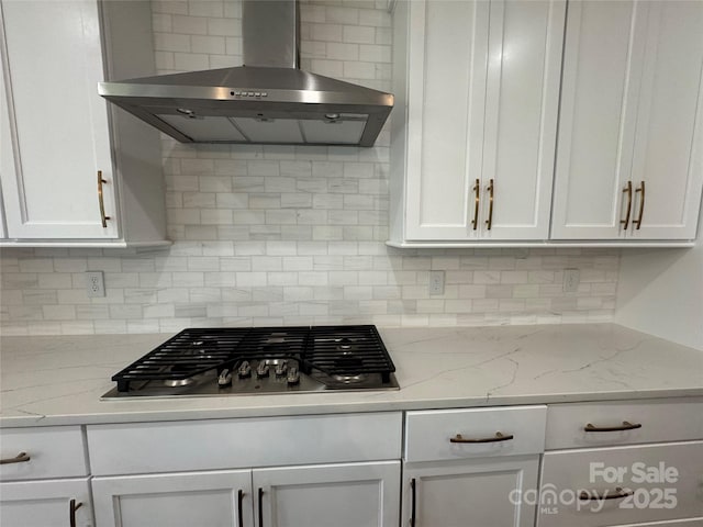 kitchen featuring white cabinets, stainless steel gas cooktop, tasteful backsplash, and wall chimney range hood
