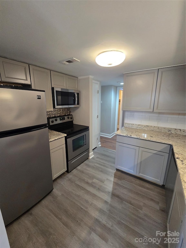 kitchen featuring gray cabinetry, appliances with stainless steel finishes, light stone countertops, light hardwood / wood-style floors, and backsplash