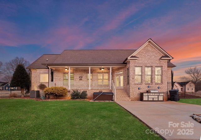 view of front of home with cooling unit, ceiling fan, a hot tub, and a lawn