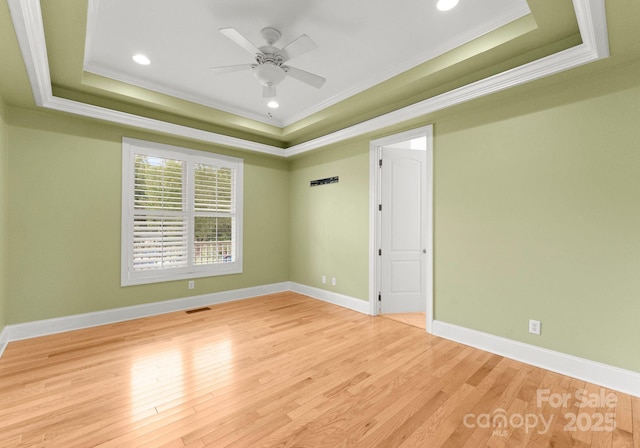 empty room featuring ceiling fan, ornamental molding, a tray ceiling, and light hardwood / wood-style floors