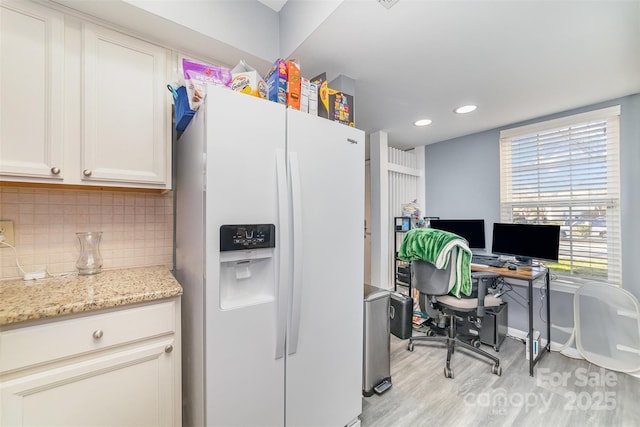 kitchen featuring backsplash, light stone counters, white refrigerator with ice dispenser, white cabinets, and light wood-type flooring