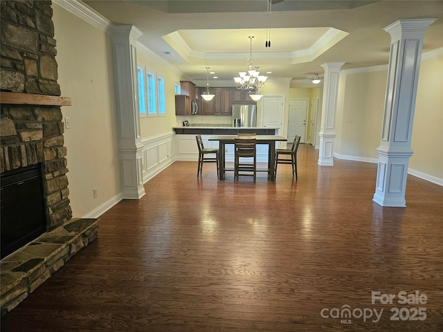 dining room featuring decorative columns, dark hardwood / wood-style flooring, a fireplace, and a tray ceiling