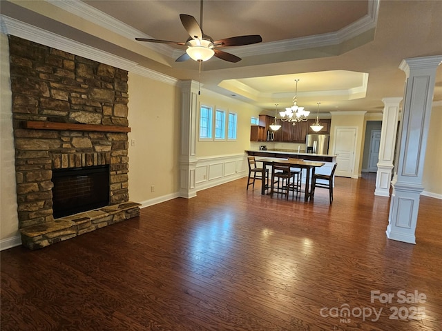 dining room featuring crown molding, decorative columns, dark hardwood / wood-style floors, a tray ceiling, and a stone fireplace