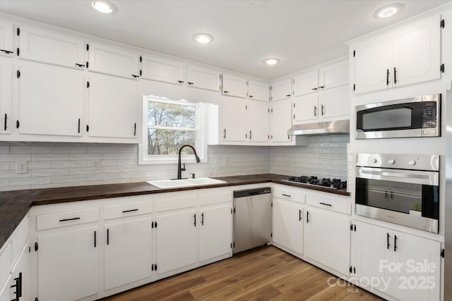 kitchen with appliances with stainless steel finishes, hardwood / wood-style floors, tasteful backsplash, white cabinetry, and sink