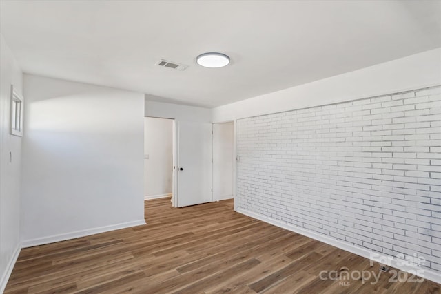 spare room with dark hardwood / wood-style flooring and brick wall