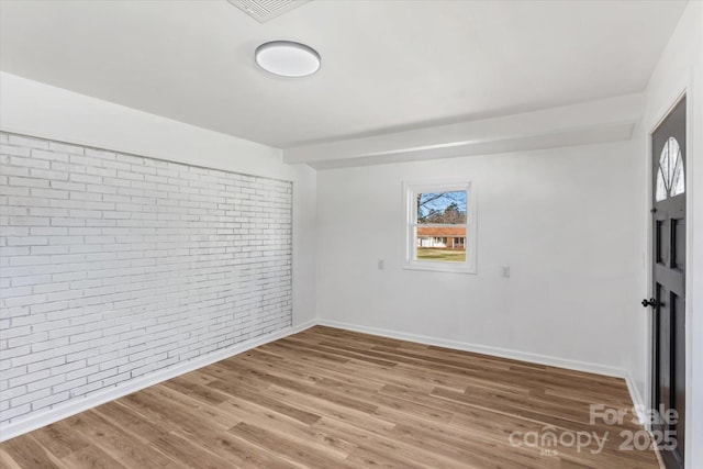 spare room featuring wood-type flooring and brick wall