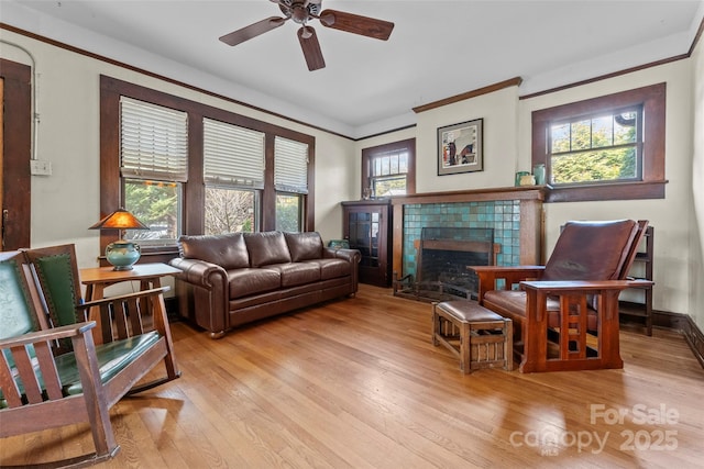 living room with crown molding, ceiling fan, a fireplace, and light wood-type flooring