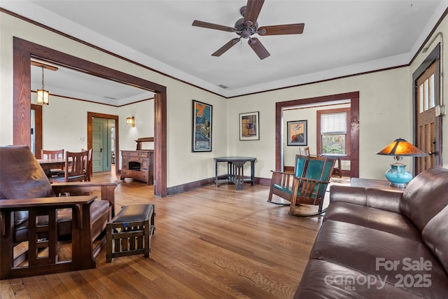 living room with ceiling fan, ornamental molding, wood-type flooring, and a fireplace