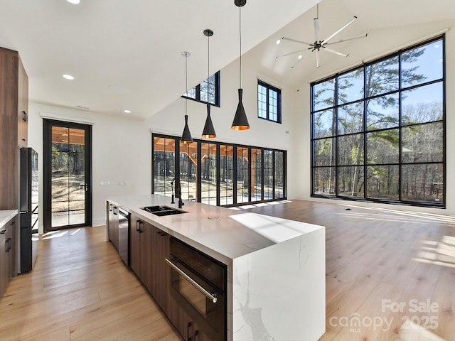 kitchen with pendant lighting, sink, a large island, stainless steel dishwasher, and light wood-type flooring