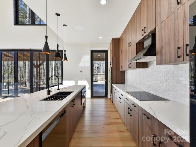 kitchen with wall chimney exhaust hood, sink, pendant lighting, light stone countertops, and black appliances