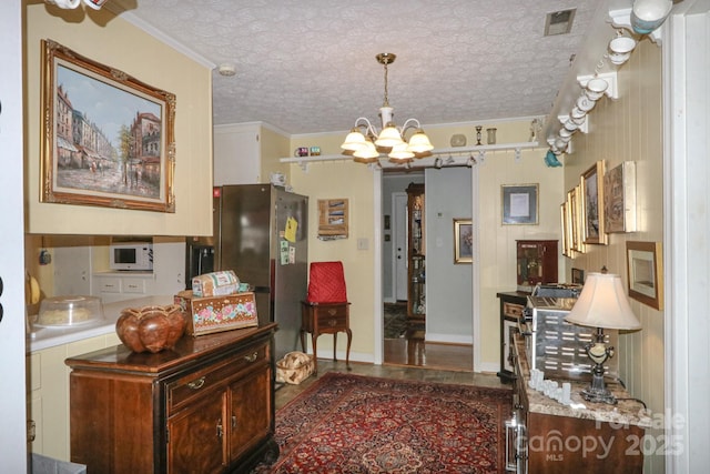 interior space with pendant lighting, stainless steel refrigerator, ornamental molding, a textured ceiling, and an inviting chandelier