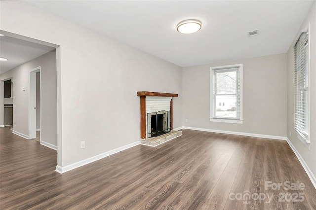 unfurnished living room with visible vents, baseboards, a brick fireplace, and dark wood finished floors