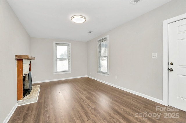 unfurnished living room with visible vents, a brick fireplace, dark wood-type flooring, and baseboards