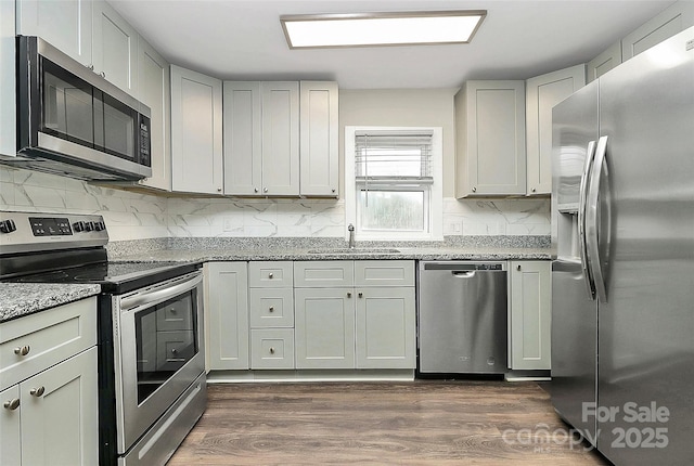 kitchen featuring light stone countertops, a sink, stainless steel appliances, dark wood-type flooring, and tasteful backsplash