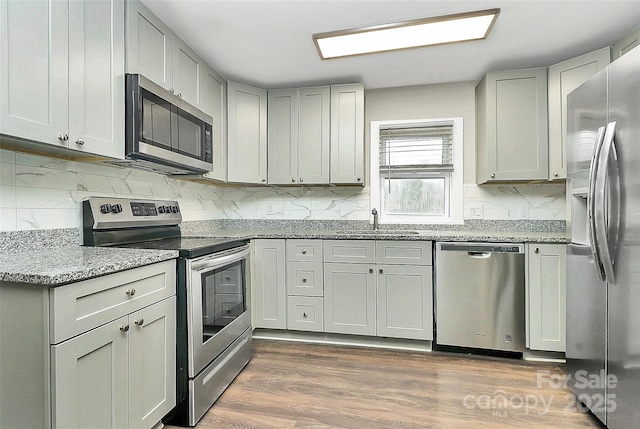 kitchen featuring dark wood-type flooring, a sink, light stone counters, tasteful backsplash, and stainless steel appliances