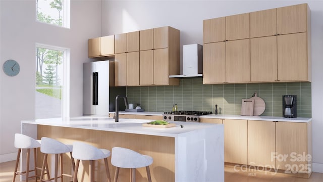 kitchen featuring wall chimney exhaust hood, a breakfast bar area, refrigerator, light brown cabinets, and decorative backsplash