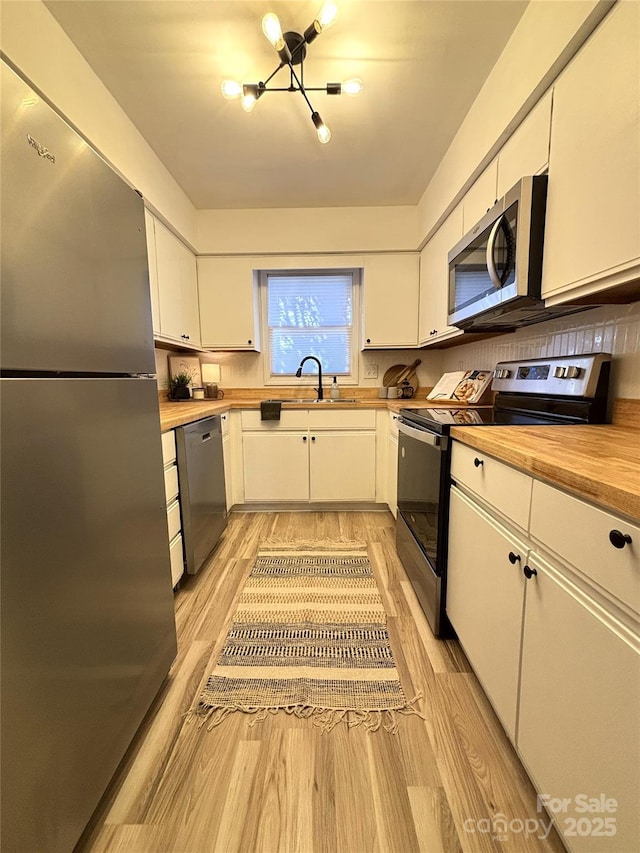 kitchen with sink, light hardwood / wood-style flooring, white cabinetry, stainless steel appliances, and a chandelier