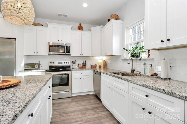 kitchen with white cabinetry, appliances with stainless steel finishes, light stone countertops, and sink