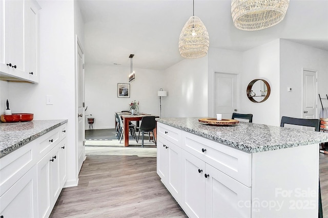 kitchen with pendant lighting, white cabinetry, a center island, light stone countertops, and light wood-type flooring