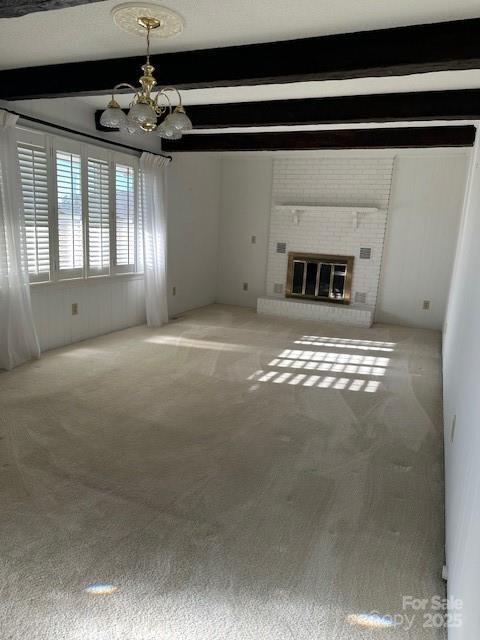 unfurnished living room featuring beamed ceiling, a chandelier, light carpet, and a fireplace