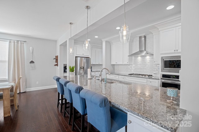 kitchen with sink, hanging light fixtures, stainless steel appliances, white cabinets, and wall chimney exhaust hood