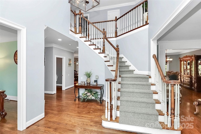 stairway with an inviting chandelier, a towering ceiling, crown molding, and hardwood / wood-style flooring