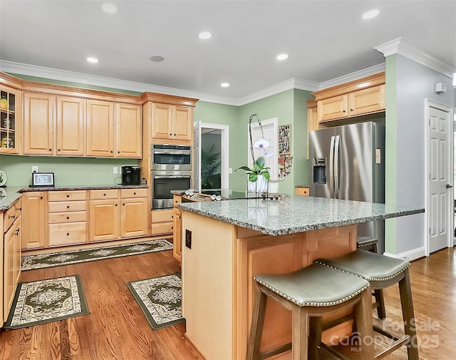 kitchen featuring appliances with stainless steel finishes, a center island, light stone counters, crown molding, and light brown cabinets