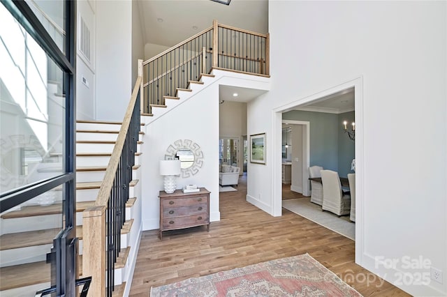 entryway featuring a high ceiling, wood-type flooring, ornamental molding, and an inviting chandelier