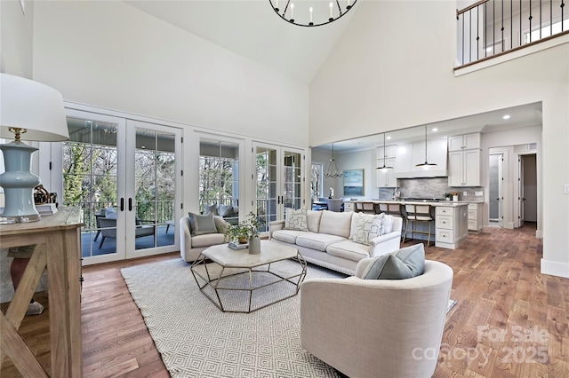 living room featuring a towering ceiling, a chandelier, light hardwood / wood-style floors, and french doors