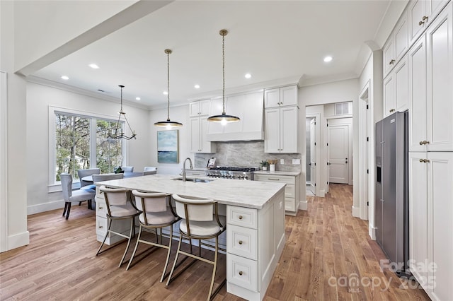 kitchen featuring sink, white cabinetry, a center island with sink, high quality fridge, and pendant lighting