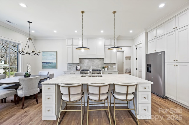 kitchen featuring white cabinetry, high end refrigerator, an island with sink, and hanging light fixtures