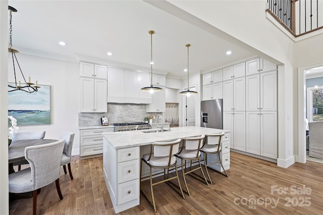 kitchen featuring decorative light fixtures, white cabinetry, a notable chandelier, stainless steel fridge with ice dispenser, and a center island with sink