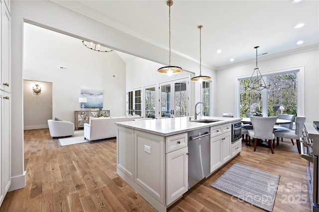 kitchen with sink, white cabinetry, hanging light fixtures, stainless steel appliances, and a kitchen island with sink