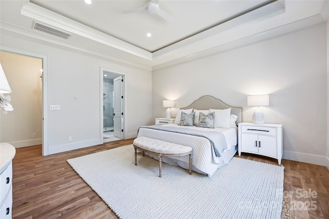 bedroom featuring wood-type flooring, ensuite bathroom, ceiling fan, and a tray ceiling