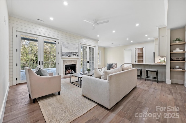 living room featuring ceiling fan, a high end fireplace, light wood-type flooring, and french doors