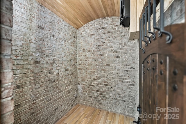 interior space featuring brick wall, hardwood / wood-style floors, and lofted ceiling