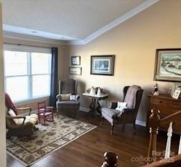 living area with dark wood-type flooring, ornamental molding, and vaulted ceiling