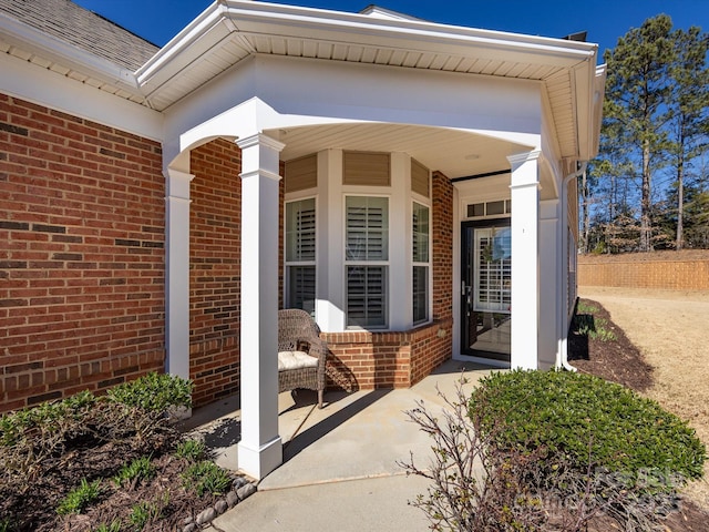 entrance to property featuring brick siding and roof with shingles