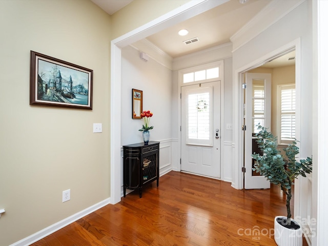 foyer entrance featuring baseboards, visible vents, wood finished floors, and ornamental molding